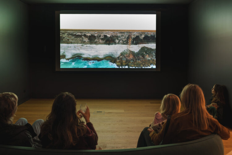 People sitting on a couch watching a screen with a view of the ocean