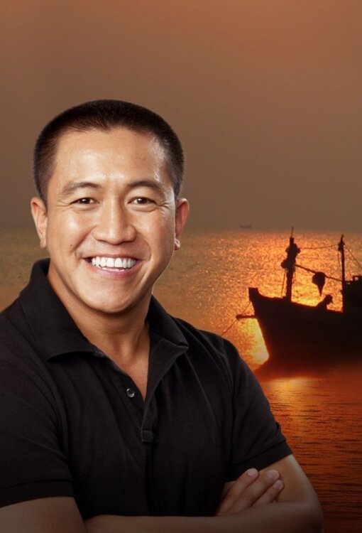 A man smiling with his arms crossed with an image of a boat and sunset in the background.